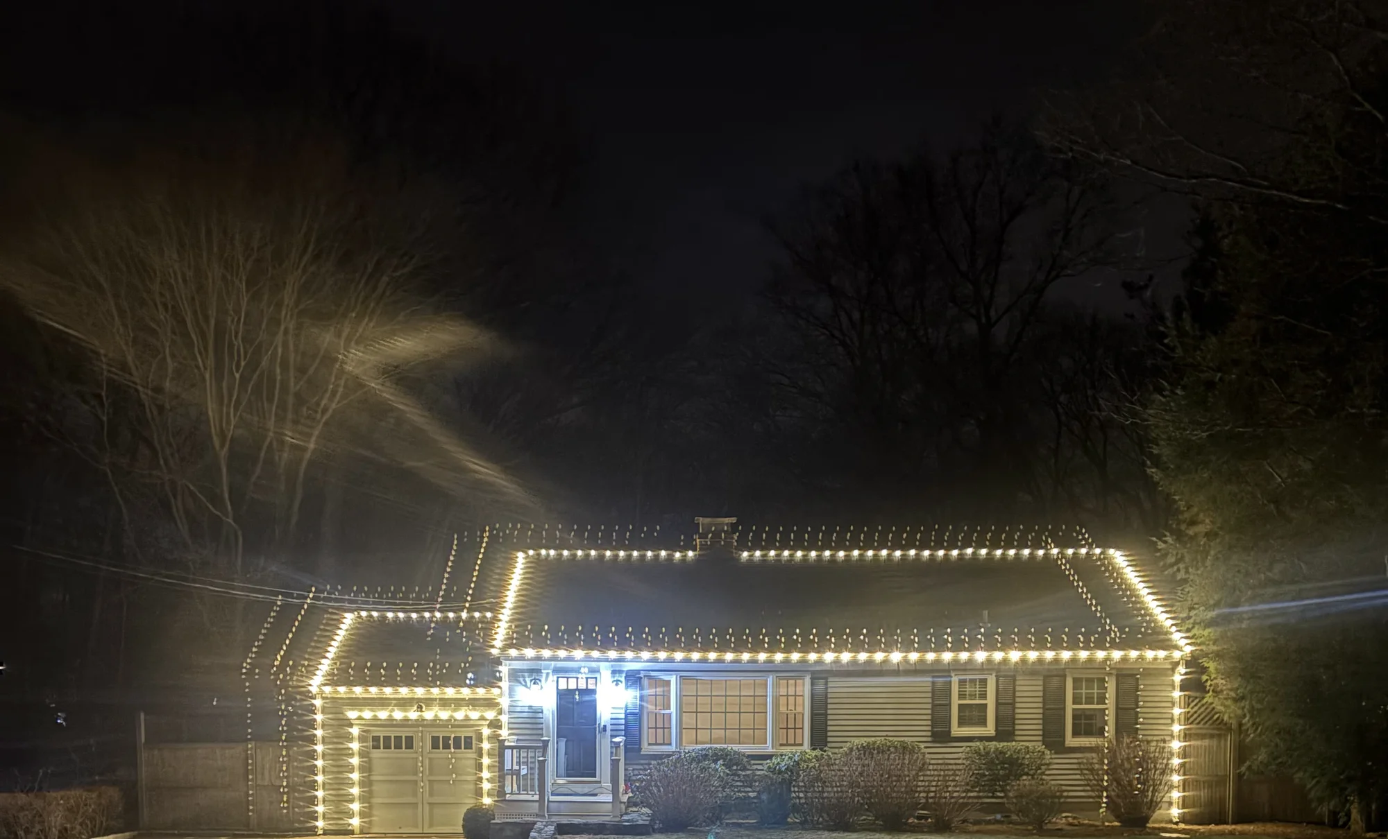 Warm white holiday lights along the roofline of a Connecticut home at dusk